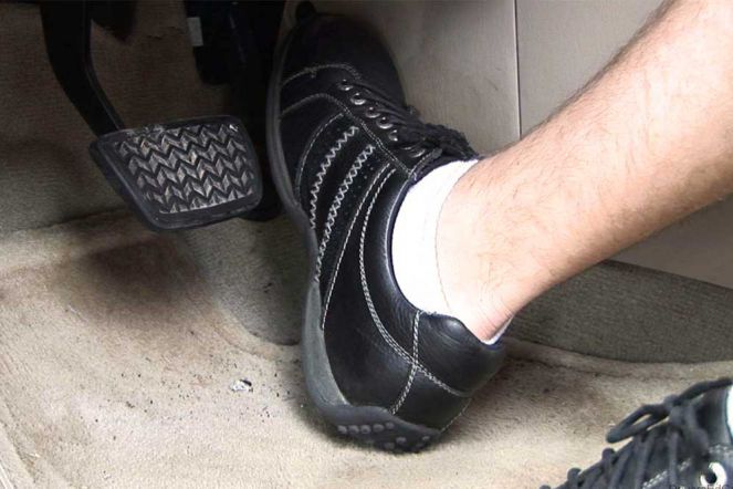 Seorang bersepatu hitam dan berkaos kaki putih sedang ingin menginjak pedal gas mobil